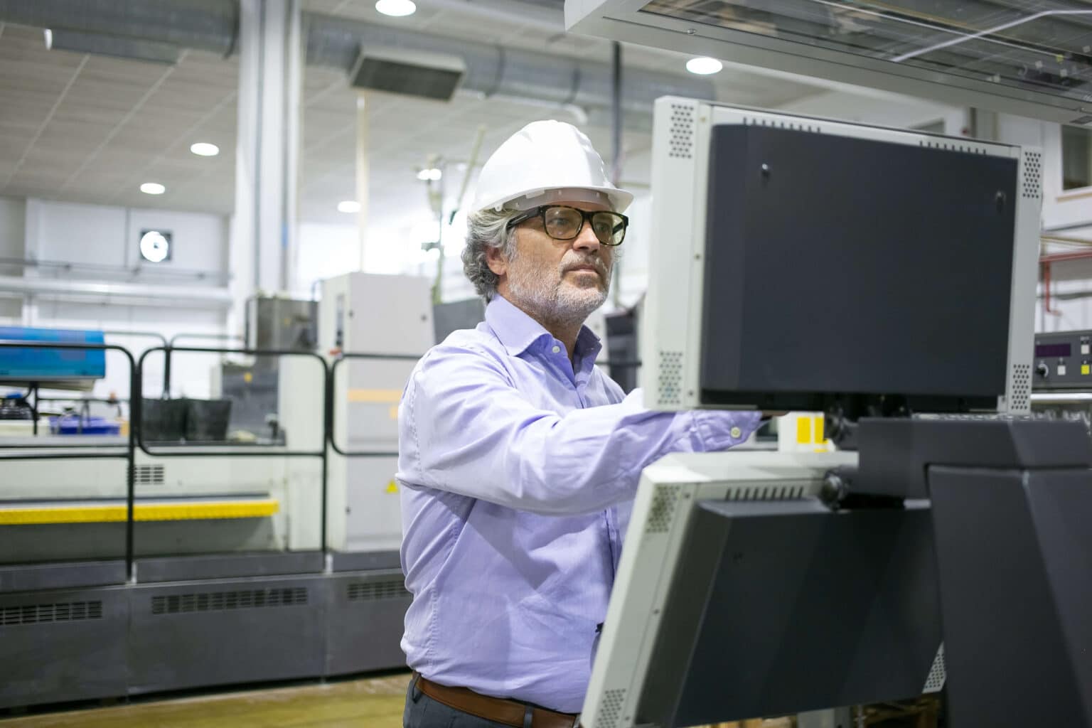 serious male plant manager hardhat glasses operating industrial machine pushing buttons control panel 1